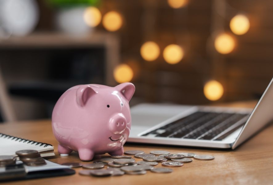 image of a pink piggy bank next to a laptop computer